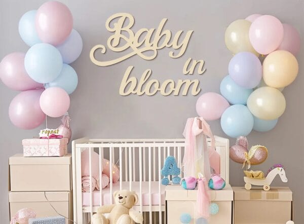 Pastel nursery decor with "Baby in Bloom" sign, crib, balloons, and toys.