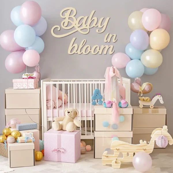 Pastel nursery decor with "Baby in Bloom" sign, crib, and gifts.
