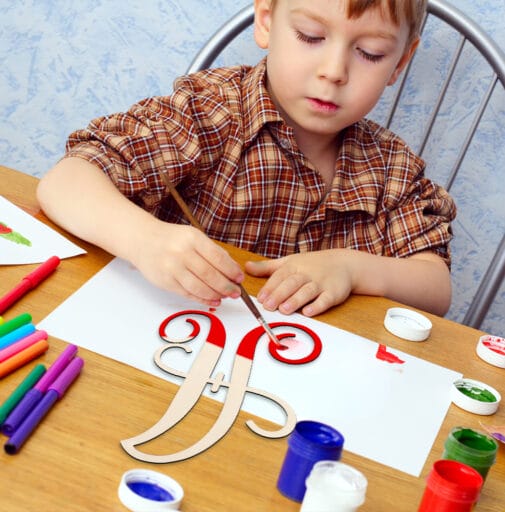 Child painting wooden letter F with red paint.